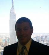 A man in suit and tie standing next to the empire state building.